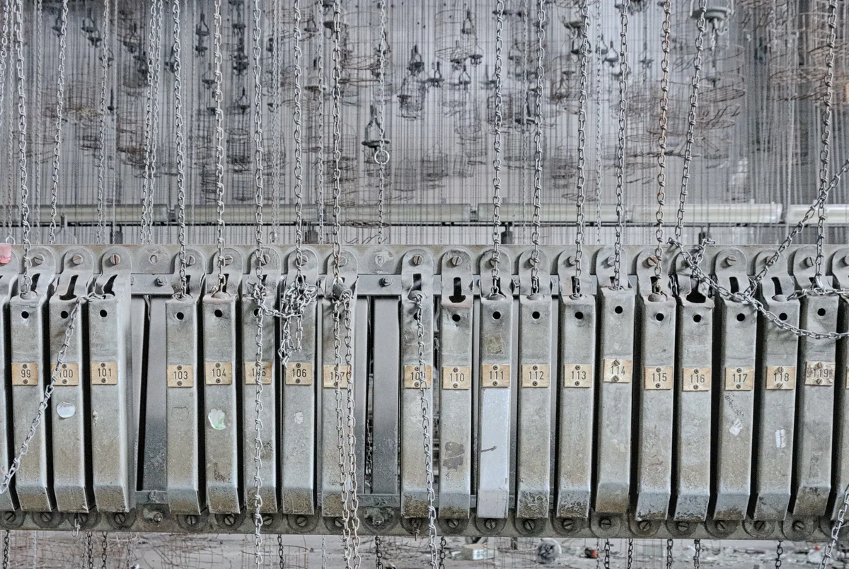 Genummerde machineonderdelen en hangende kettingen in een oude fabriek