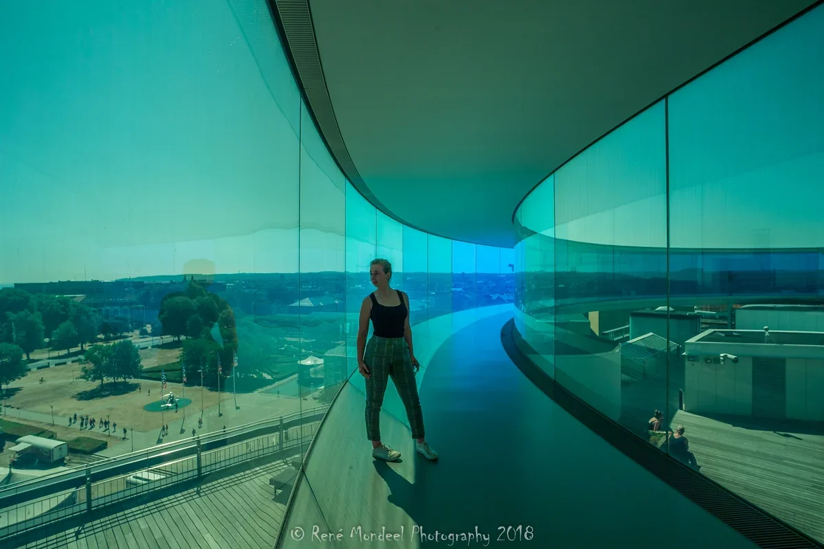 Persoon in een turquoise glazen museumgang met uitzicht over de stad